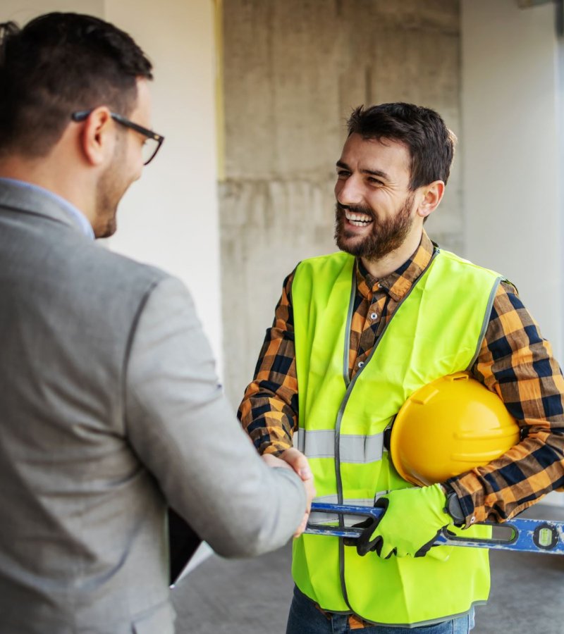 Smiling construction worker shaking hands with supervisor while standing in building in construction process.