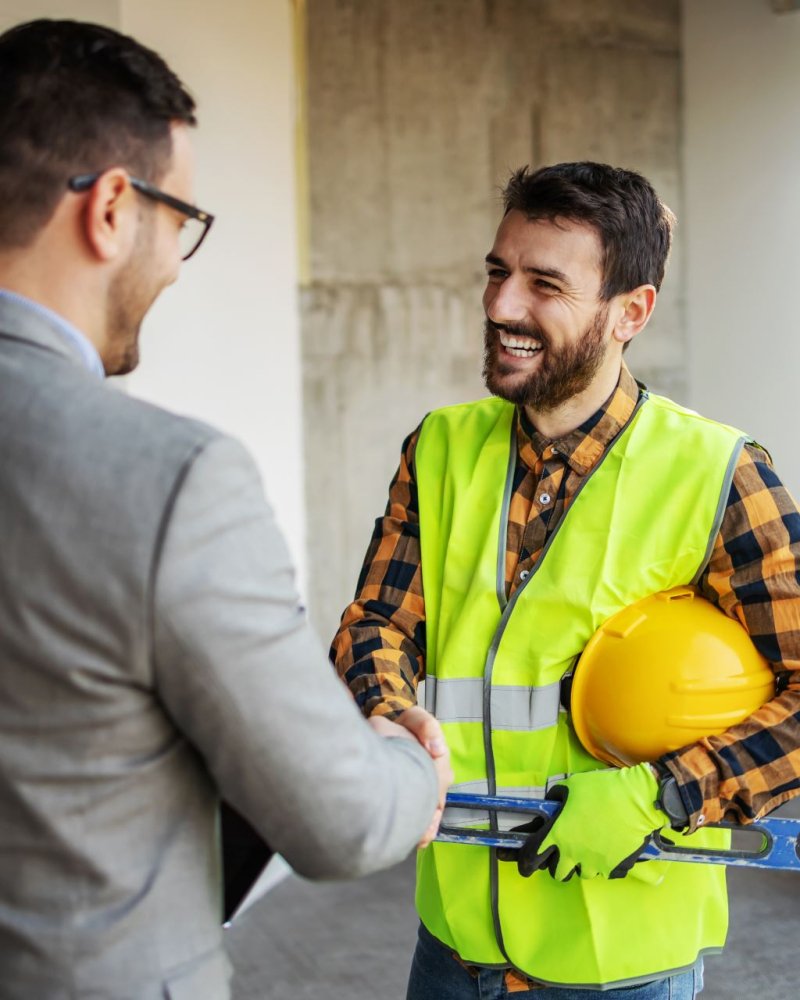 Smiling construction worker shaking hands with supervisor while standing in building in construction process.